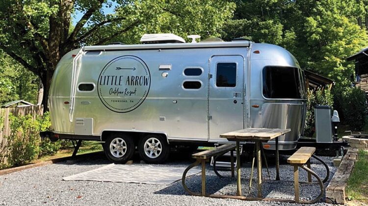 A silver camper trailer is parked in a campsite