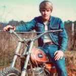 A vintage photo of a young man sitting astride a motorcycle