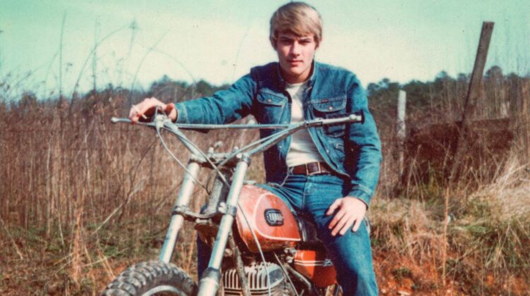 A vintage photo of a young man sitting astride a motorcycle