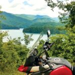 A motorcycle is in the foreground with a lake in the background