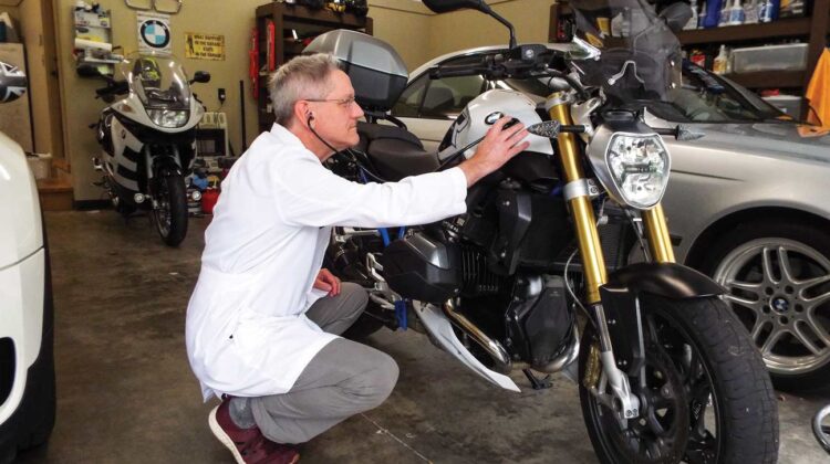 A man in a lab coat uses a stethoscope on a BMW motorcycle