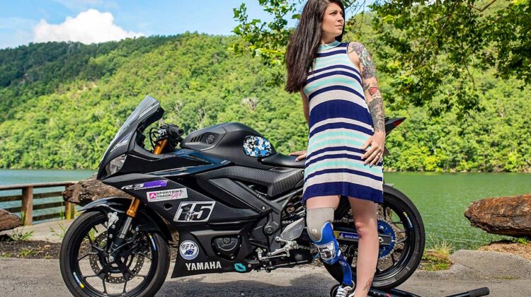 A woman leans against a sportbike on the shore of a lake.