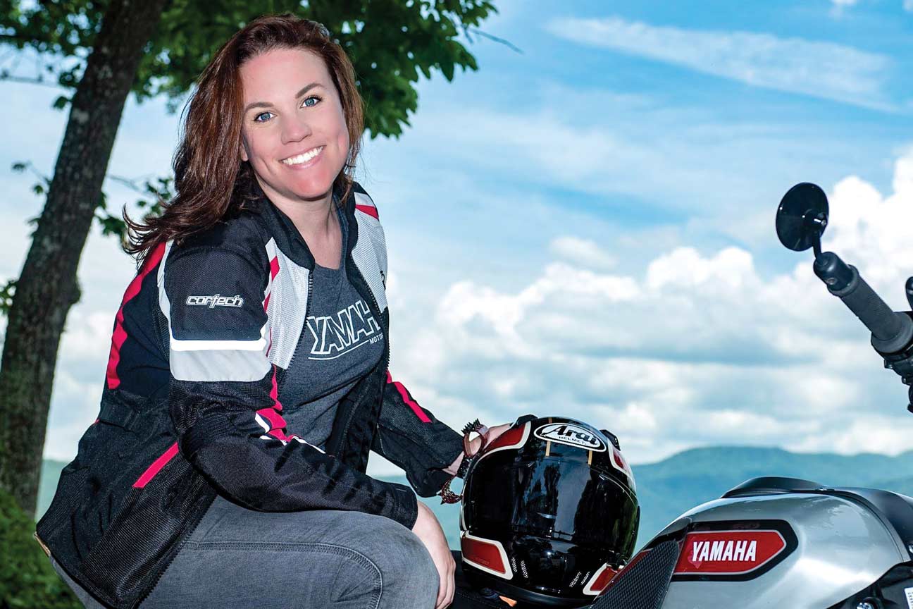 A smiling woman sits astride a Yamaha motorcycle.