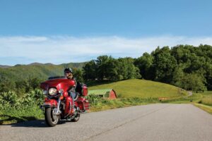 A woman rides a red Harley-Davidson through a rural setting