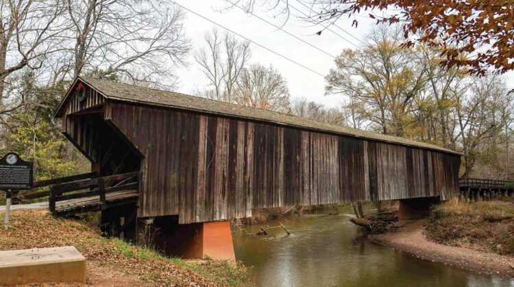 Side view of a covered bridge over a peaceful stream.