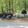 A pickup with an RV is parked in a campsite alongside a motorcycle