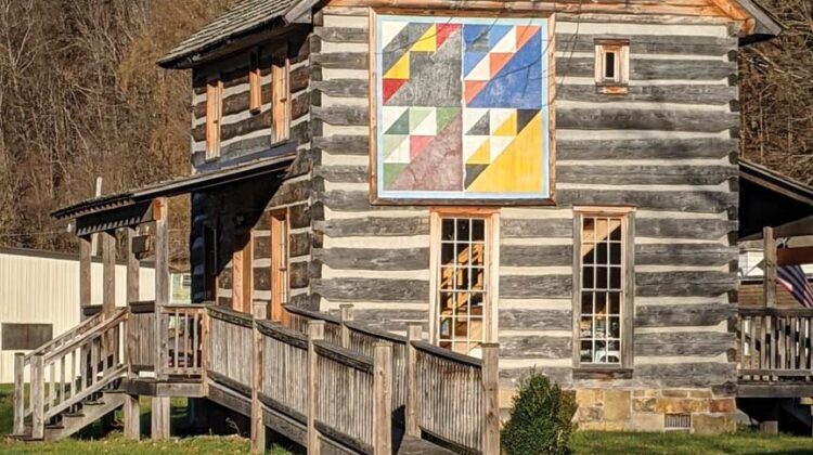 A historic log house with a large quilt square on the side