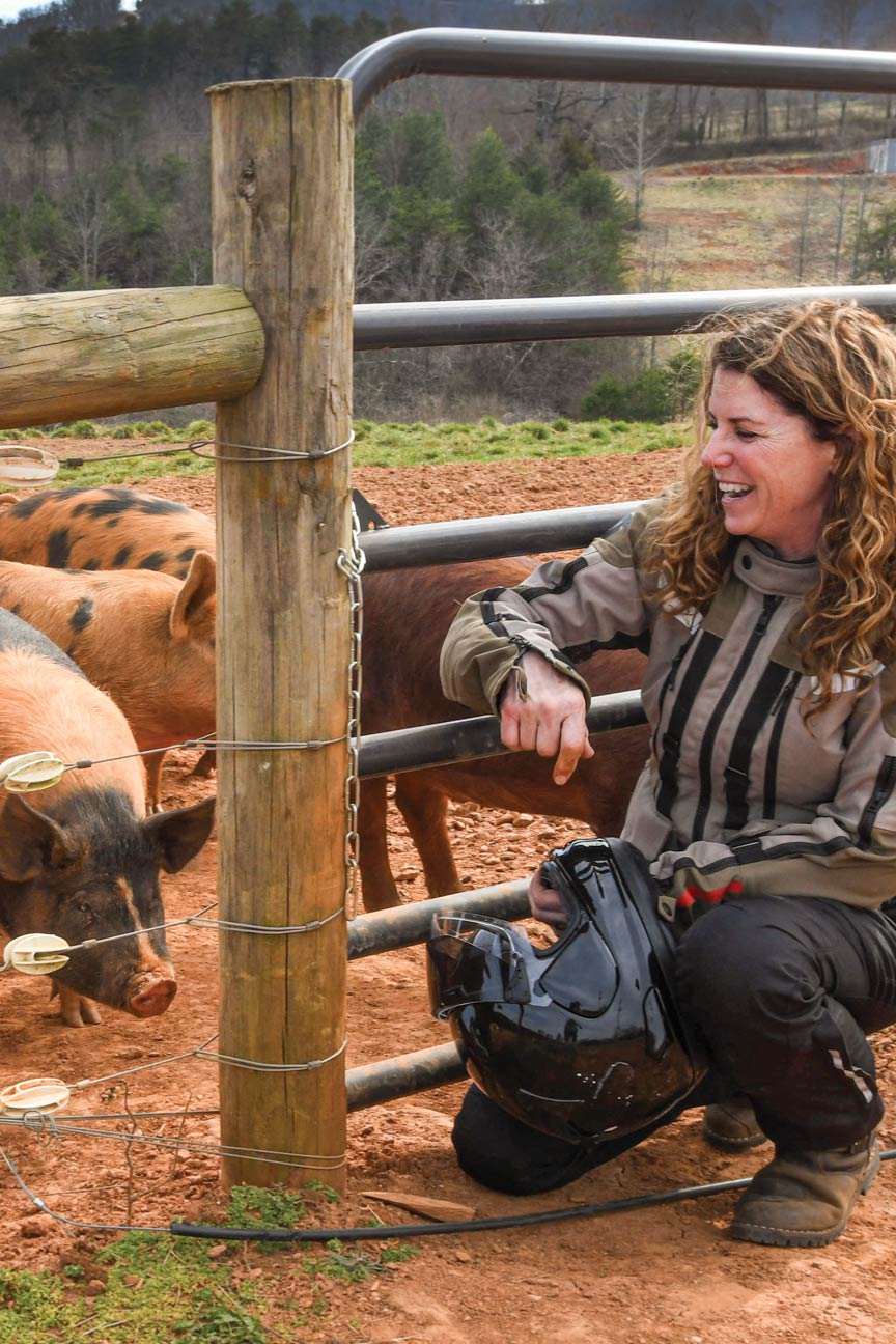 A woman in motorcycle attire sits beside a livestock pen.