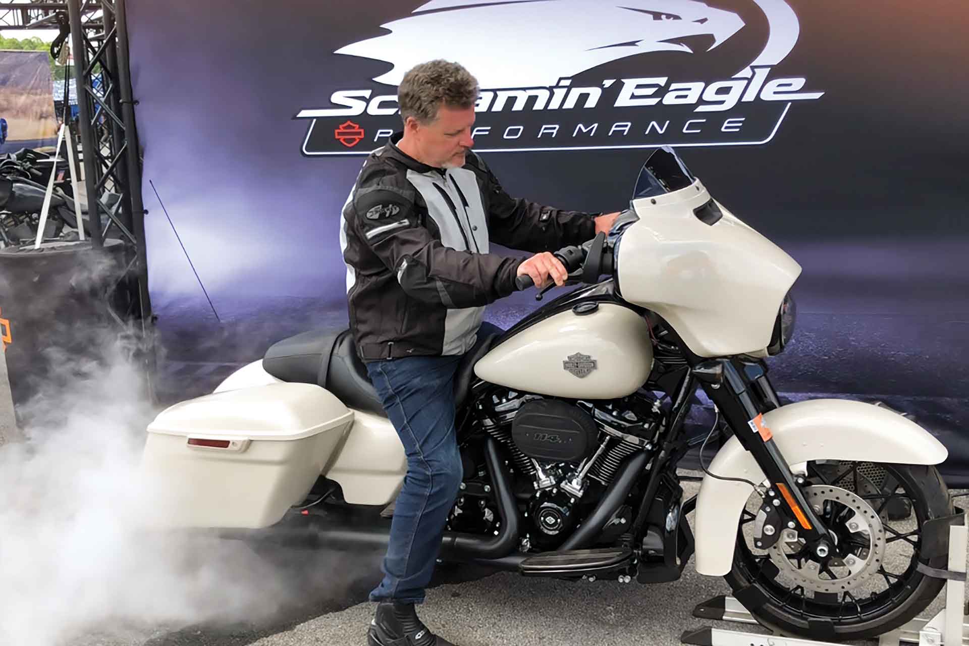 A rider practices a burnout on a white Harley-Davidson.