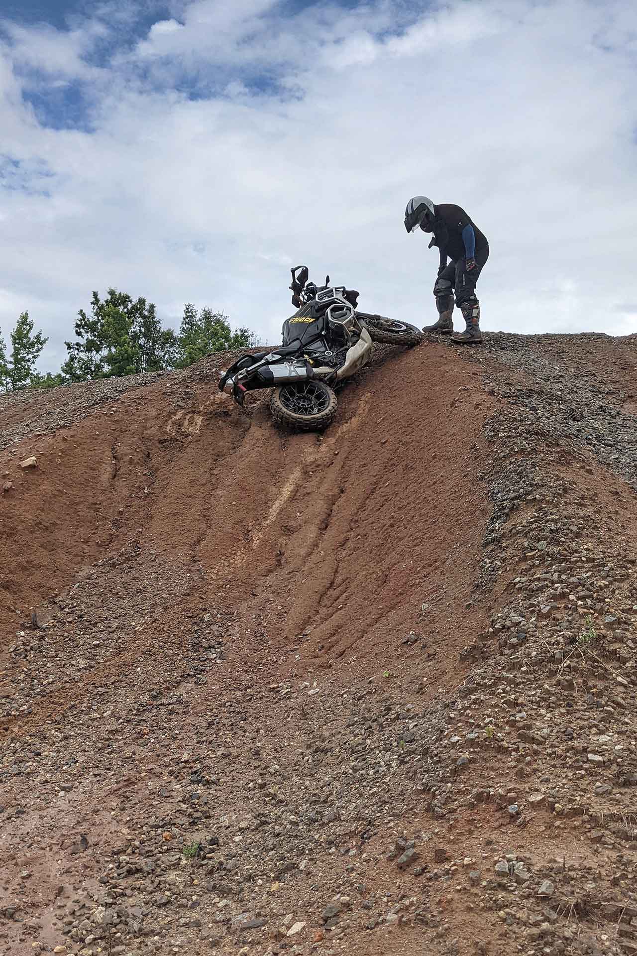 A rider stoops over to pick up his motorcycle near the top of a hill obstacle.