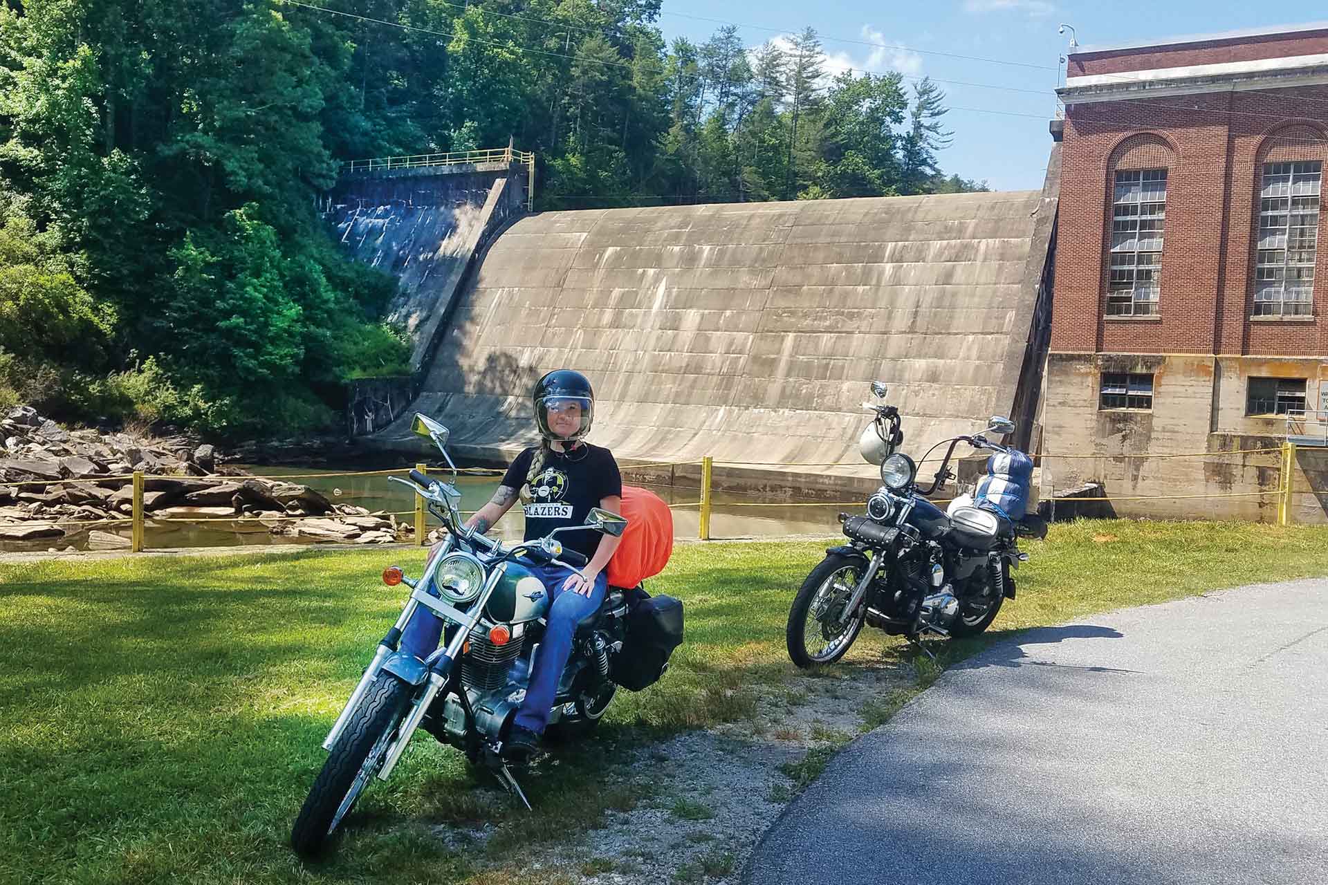 A woman sits on her motorcycle, taking a break at a dam.