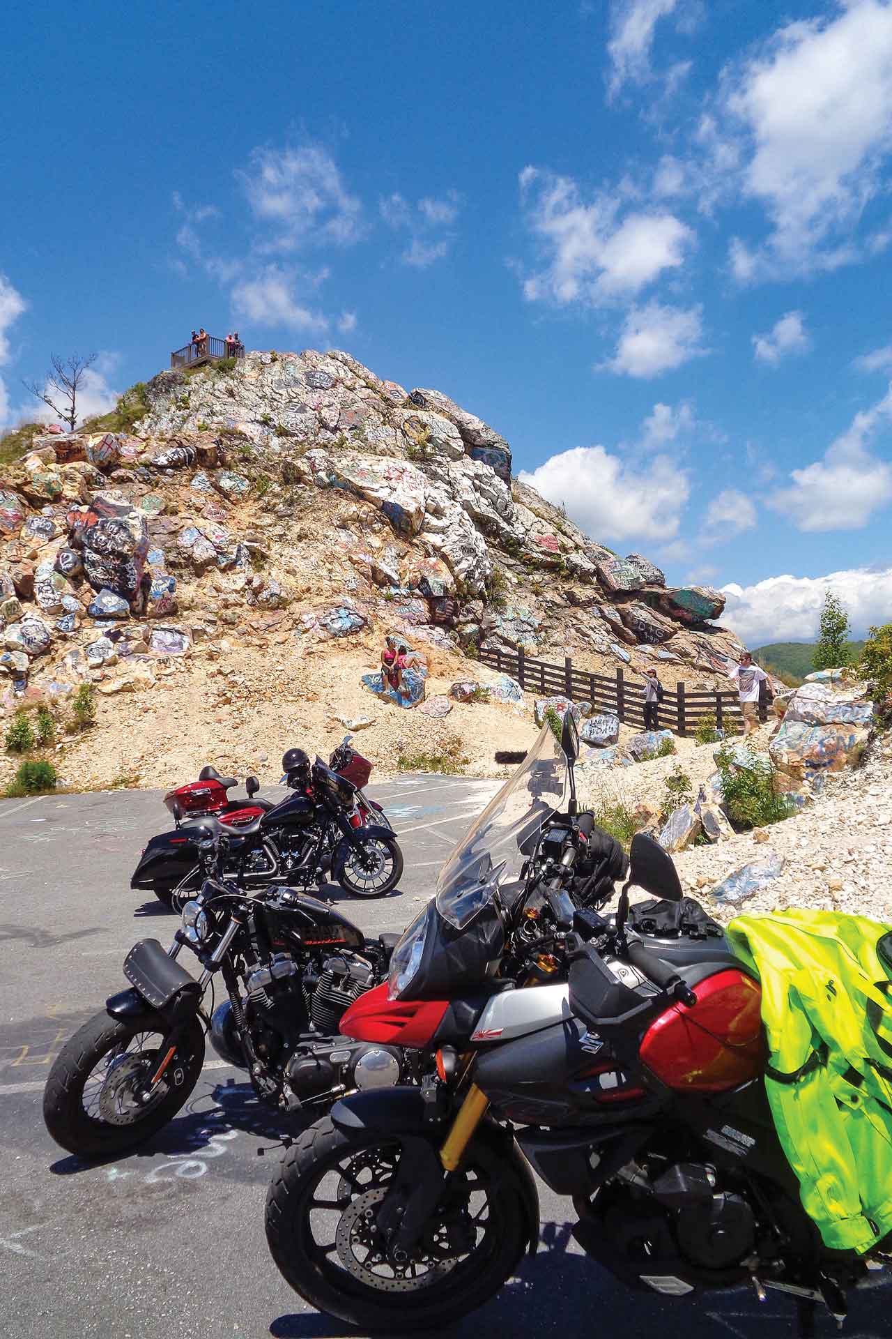 A group of motorcycles are parked in front of a craggy hillside covered in graffiti.