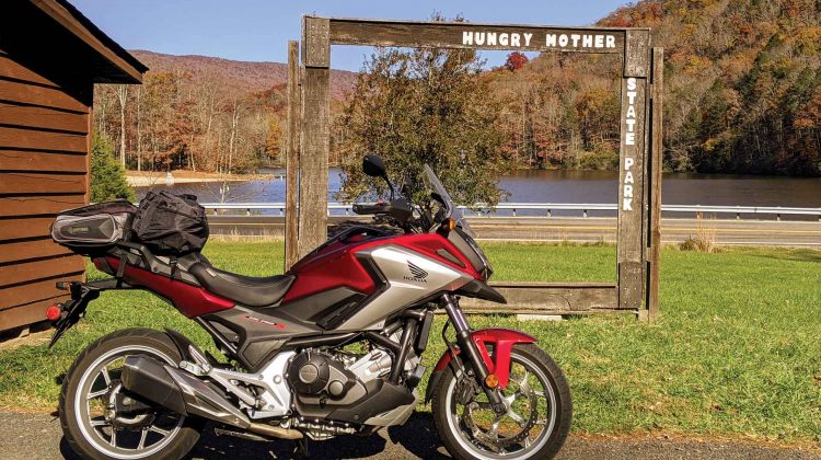 A red and silver Honda motorcycle is parked at the entrance to a state park.