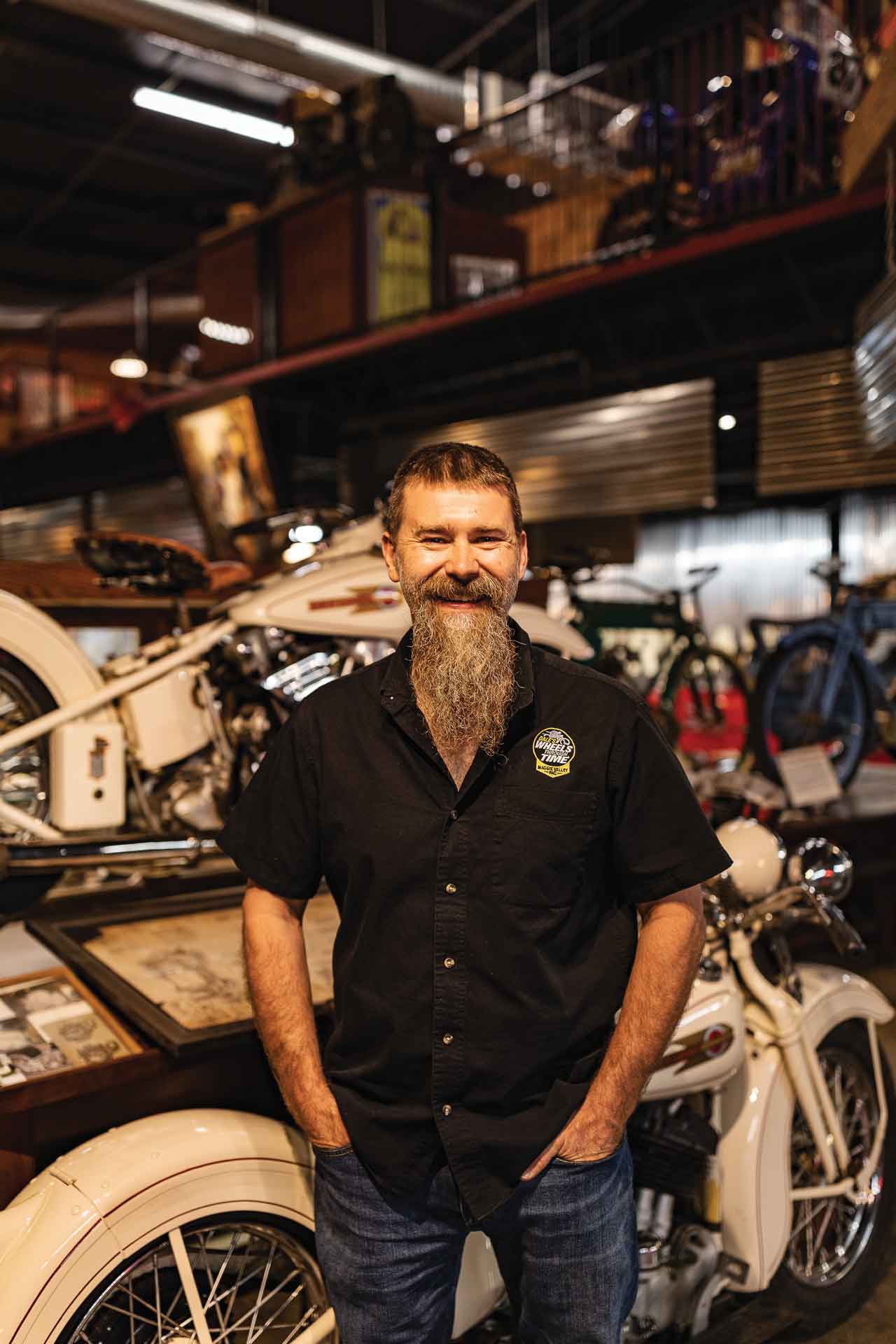 A man stands with an antique motorcycle in a museum.