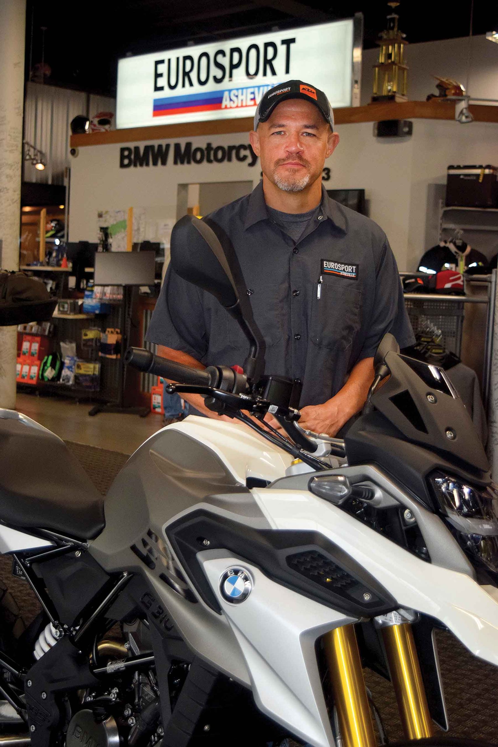Eurosport Asheville owner Thomas Montgomery stands in a showroom beside a silver BMW motorcycle