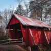 A red covered bridge stands amid leafless winter trees