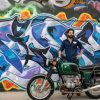 A man stands with a vintage BMW motorcycle in front of a colorful graffiti mural
