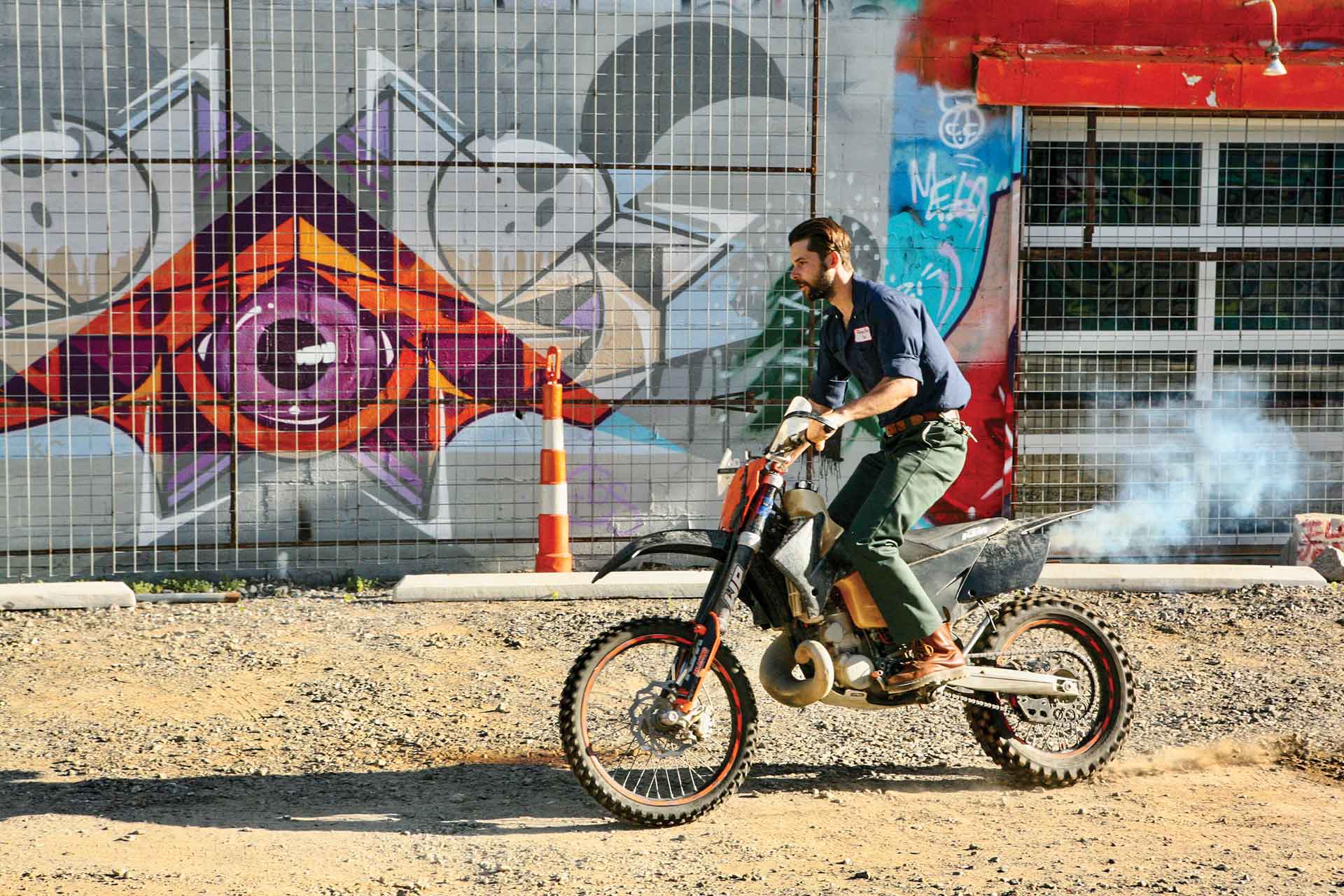 A man rides a vintage dirtbike in a gravel parking lot